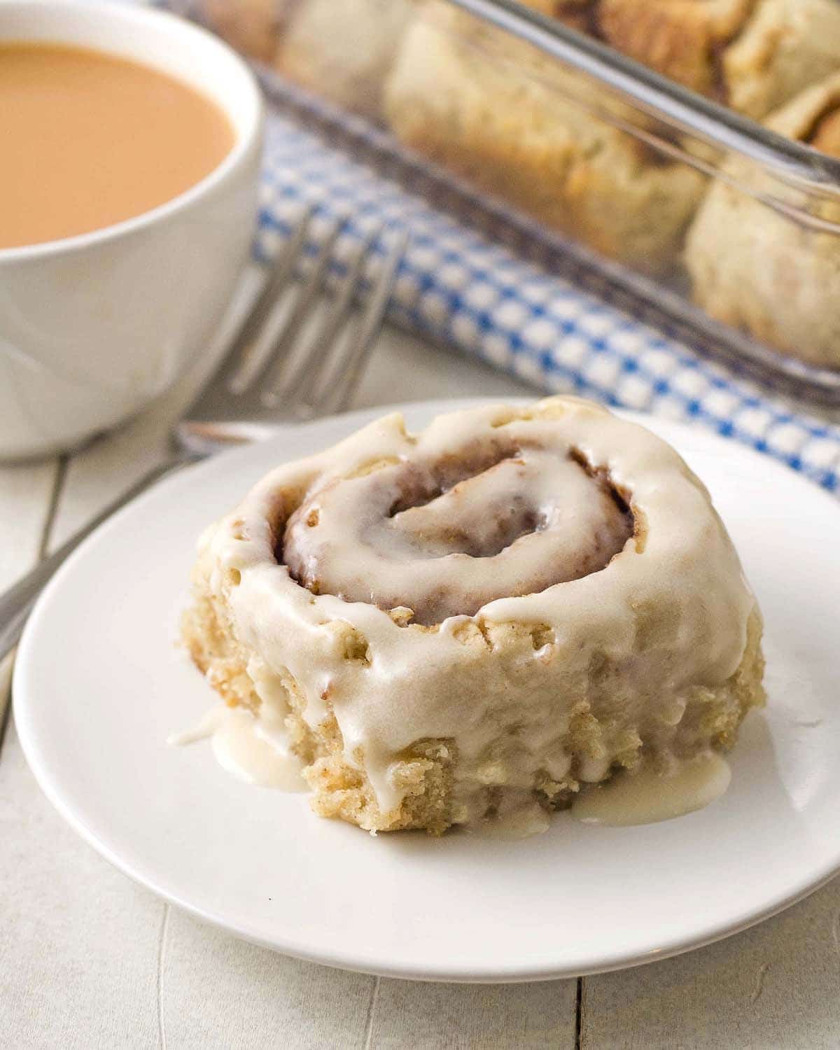 An overhead shot of a eggless cinnamon roll on a plate, roll is topped with icing.