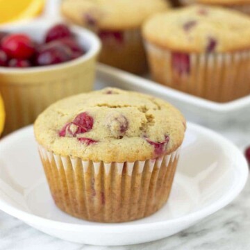 An orange cranberry muffin on a small plate, fresh cranberries are on both sides of the plate.