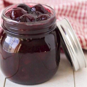 A mason jar of cherry sauce on a white table, the jar lid is leaning against the jar.
