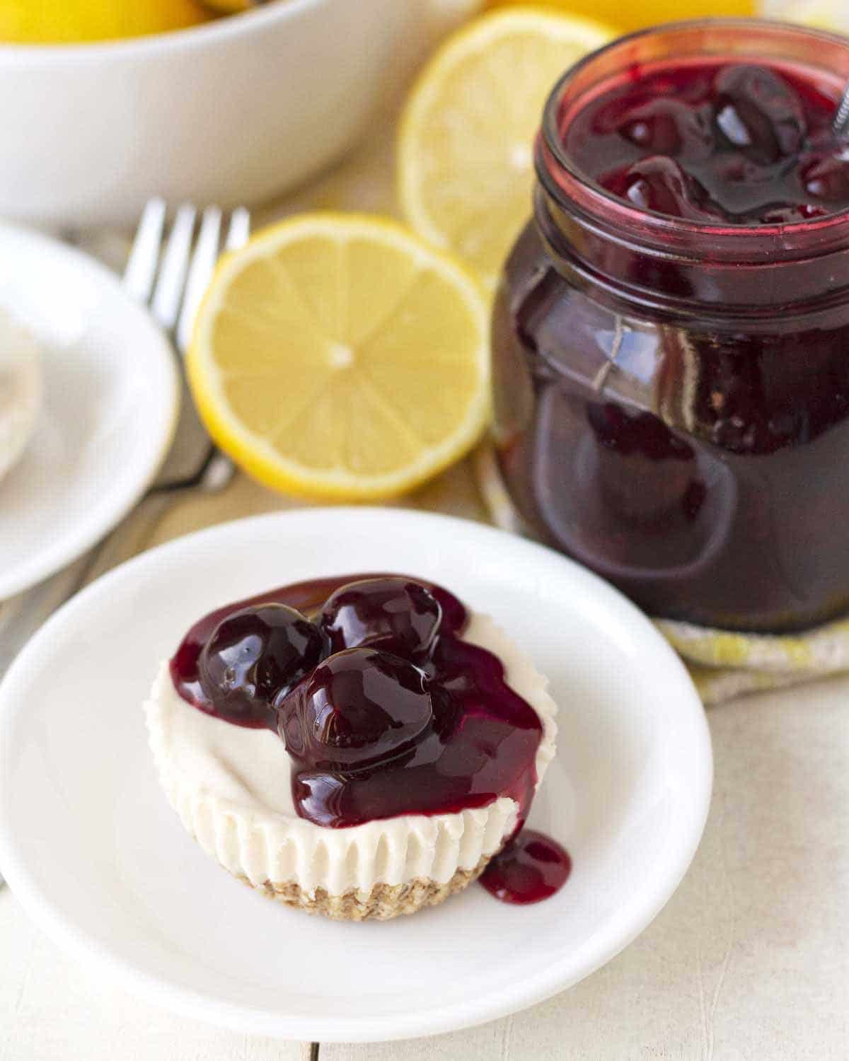 A mini lemon cheesecake on is white plate, cheesecake is topped with cherry sauce.