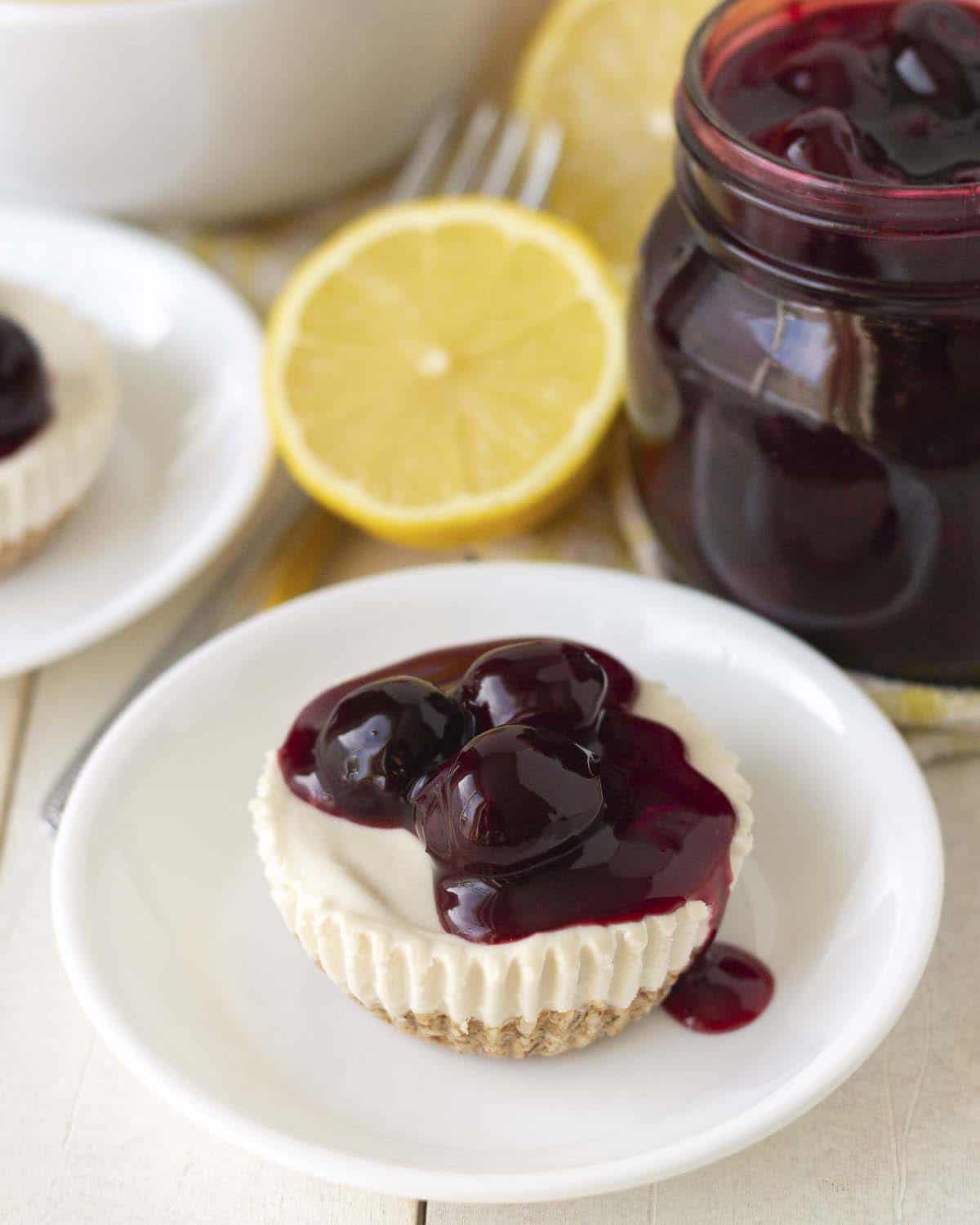 A mini vegan lemon cheesecake, topped with cherry sauce, on a small white plate.
