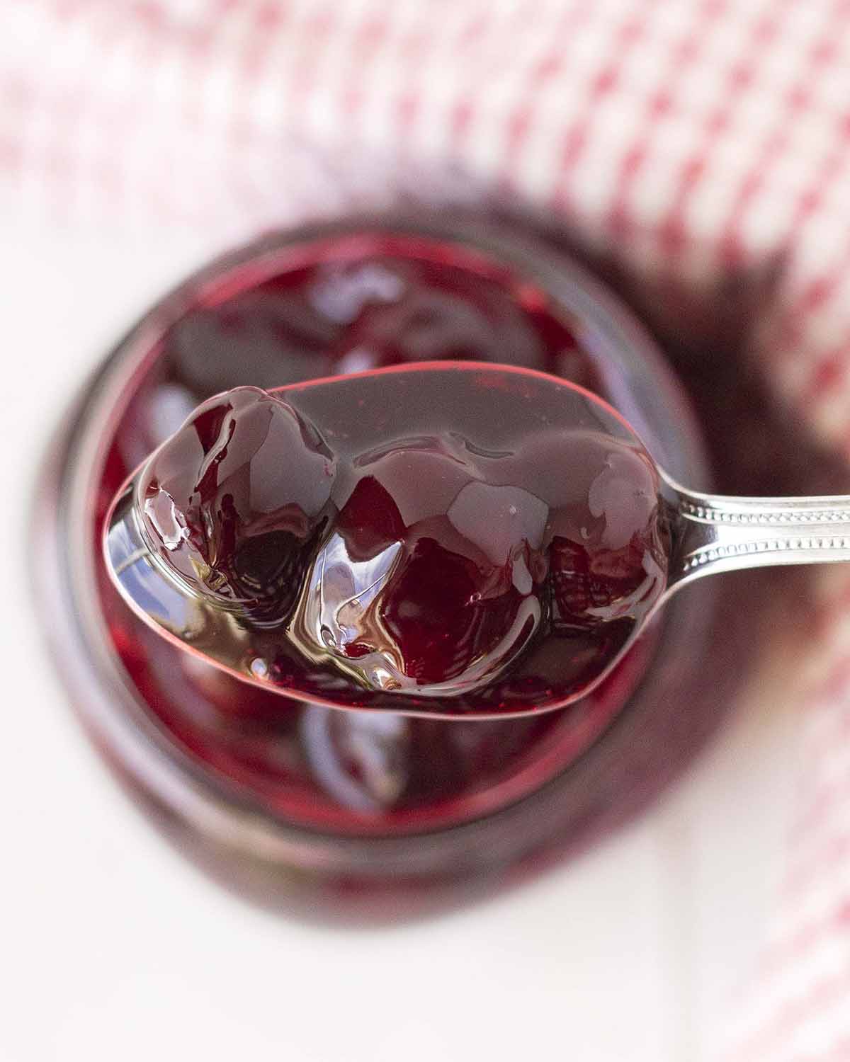 A close up shot of a spoon filled with cherry topping.