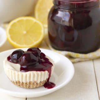 An egg-free lemon cheesecake bite on a small white plate, cheesecake is topped with cherry sauce.