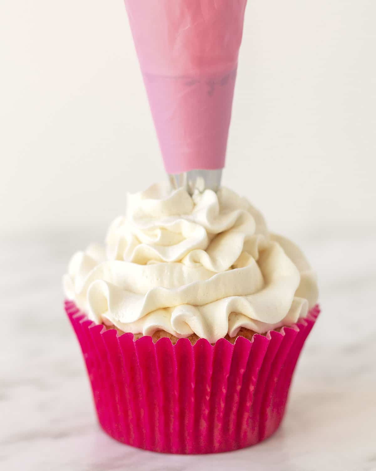 Image shows vegan buttercream being piped onto a vanilla cupcake.