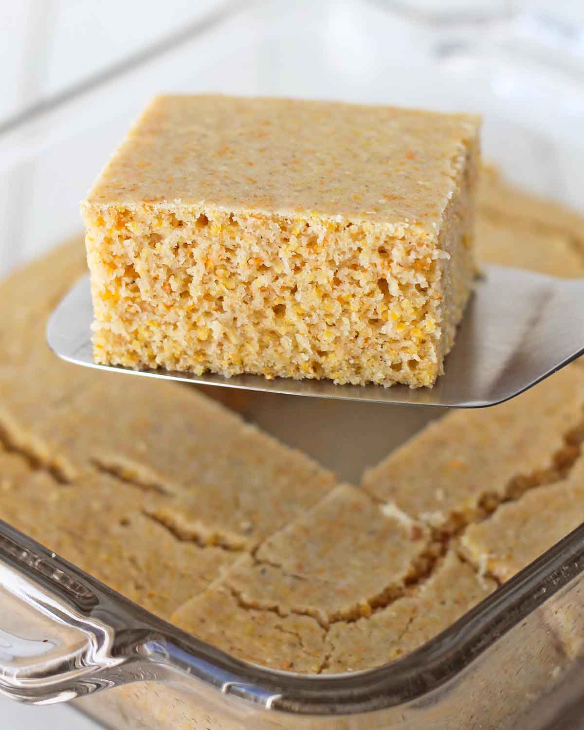 A square slice of eggless cornbread lifted out of the baking dish with a metal spatula.