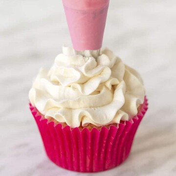Vanilla frosting being piped onto a cupcake using a pink coloured piping bag.