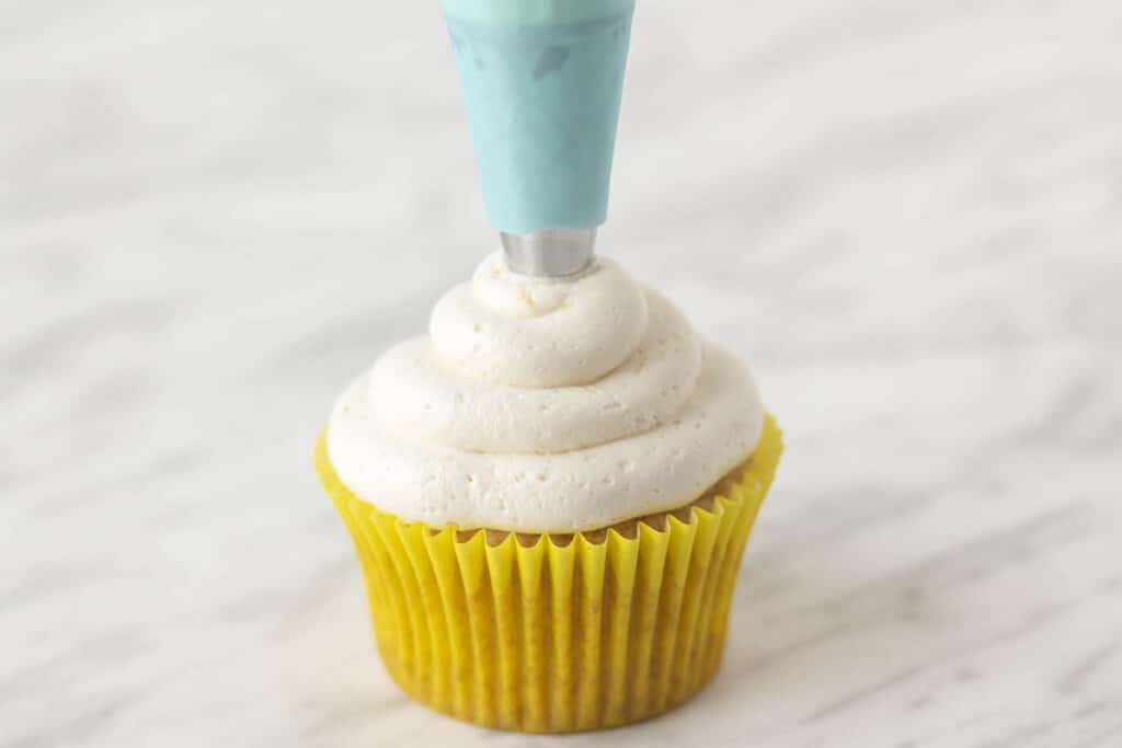 Lemon frosting being piped onto a cupcake using a blue coloured piping bag.
