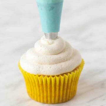 Lemon frosting being piped onto a cupcake using a blue coloured piping bag.