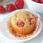 A strawberry muffin on a small plate with the muffin wrapper peeled down.