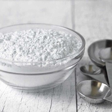 A glass bowl filled with baking powder sitting on a white wood surface.