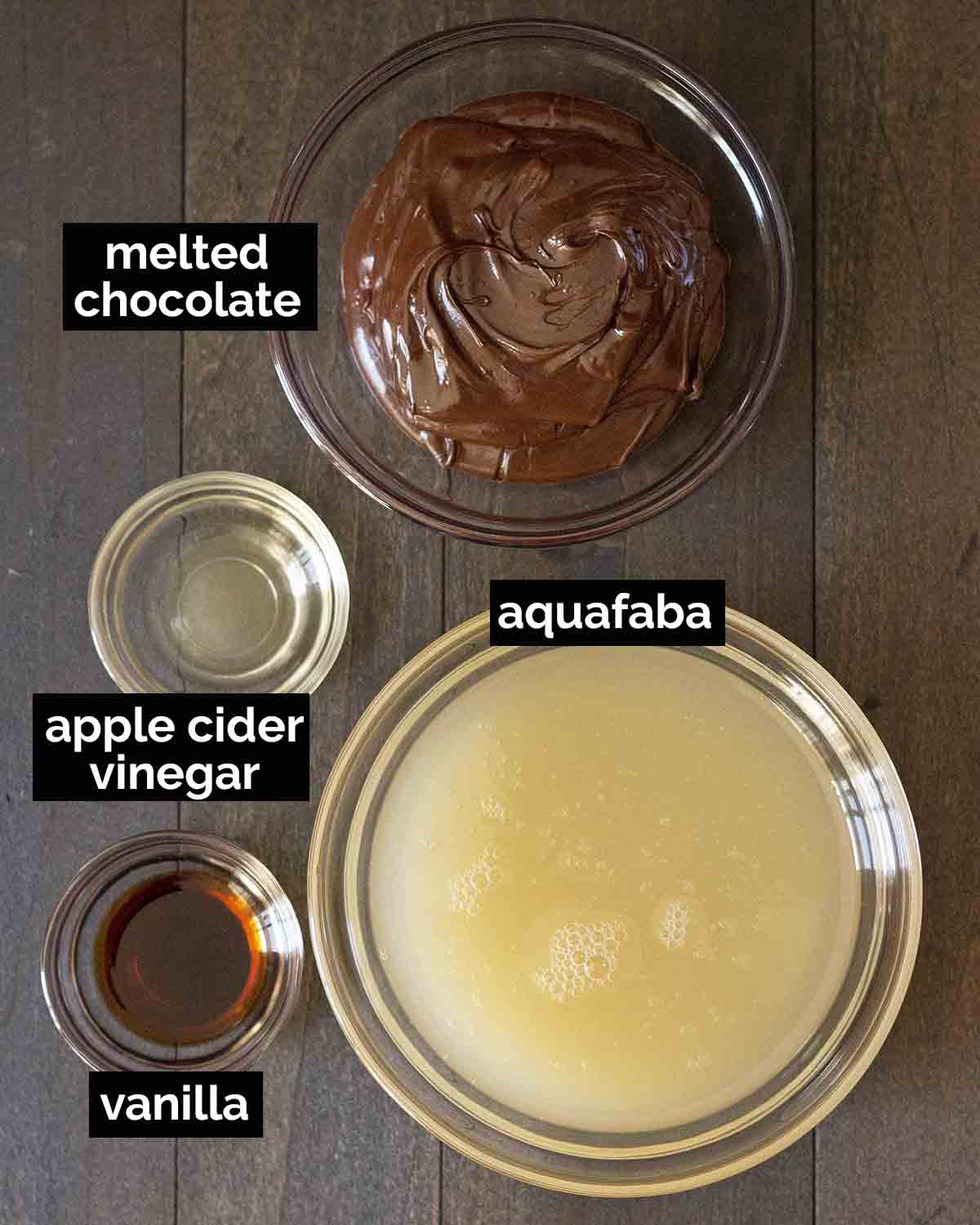 Overhead shot of the four ingredients needed to make aquafaba chocolate mousse (chocolate, aquafaba, vinegar, and vanilla).