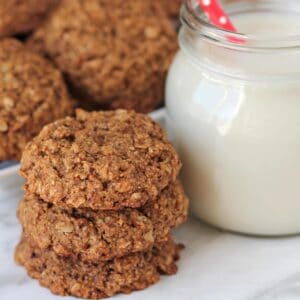 A stack of three oatmeal cookies sitting beside a glass of milk.