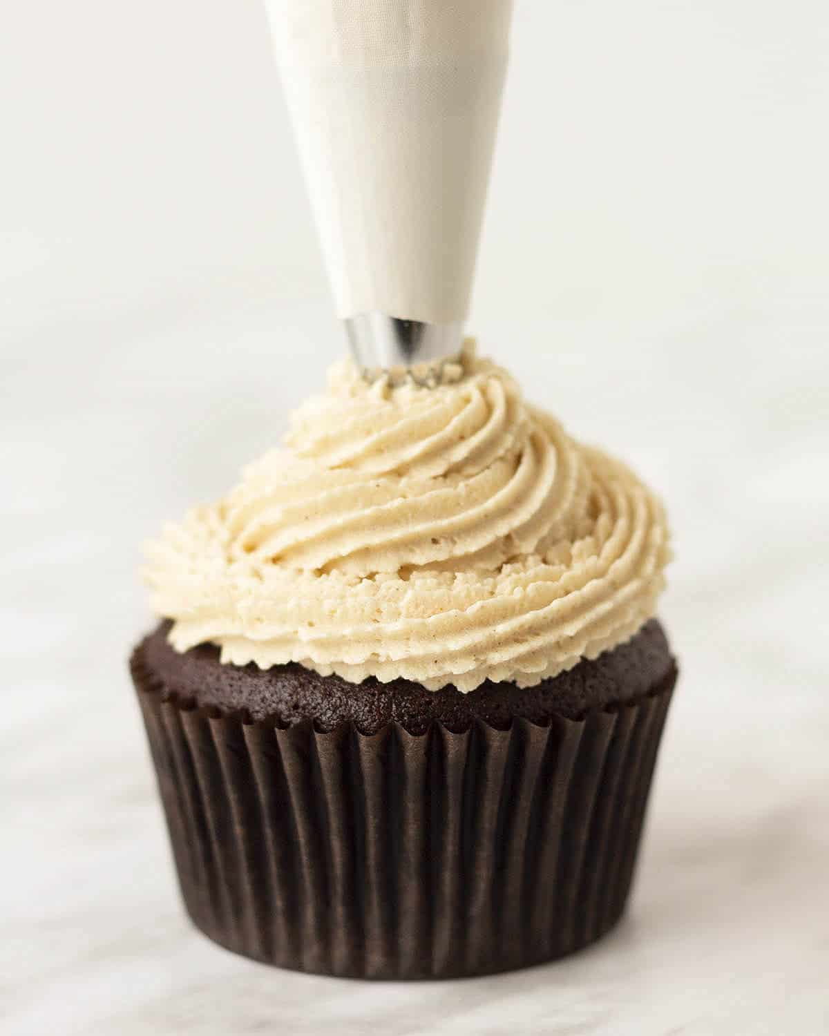Dairy-free peanut butter icing being piped onto a chocolate cupcake.