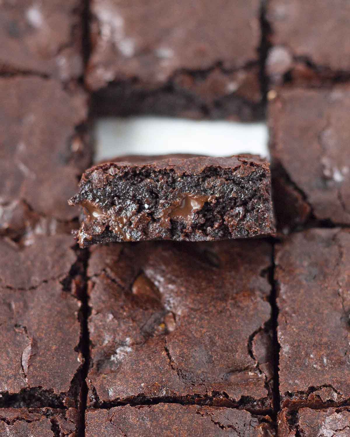 Image shows nut-free vegan gluten-free brownies, one brownie is tilted up to show the fudgy inside and melty chocolate chips.