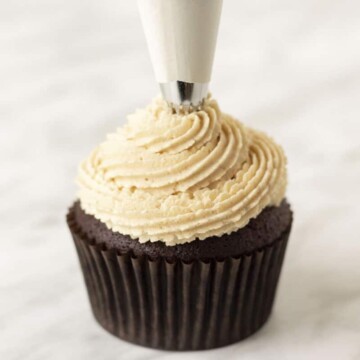 Peanut butter frosting being piped onto a cupcake with a piping bag.