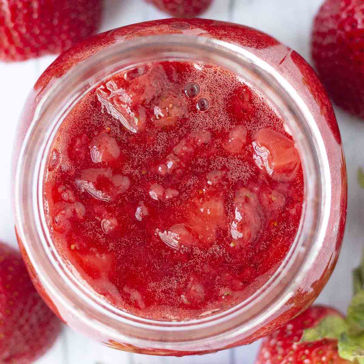 An overhead shot of homemade strawberry sauce in a glass jar.