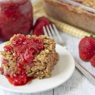 A slice of baked berry oatmeal on a white plate, oatmeal is topped with strawberry sauce.