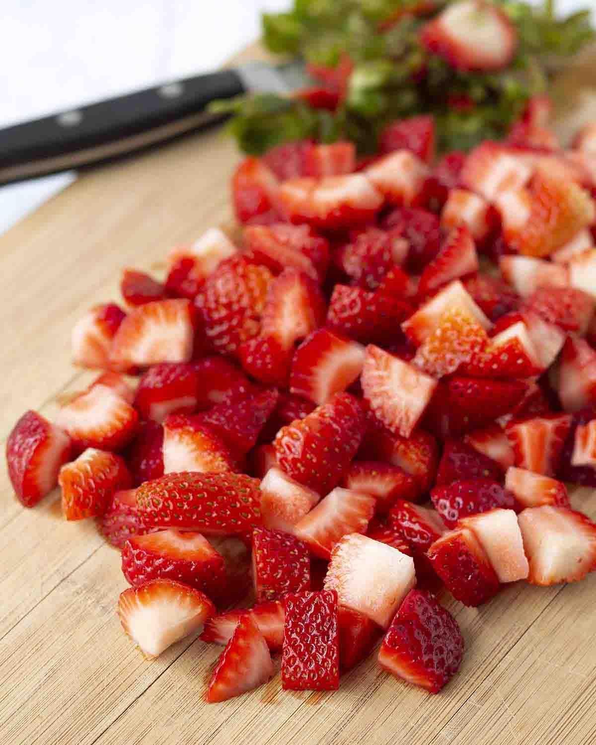 Chopped fresh strawberries on a bamboo cutting board.