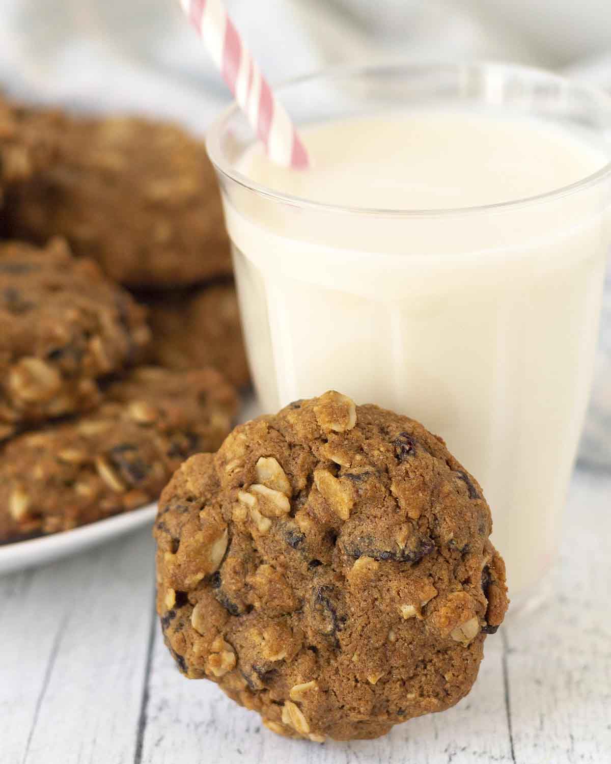 An oatmeal cookie leaning against a glass of almond milk, the glass has a pink straw in it.