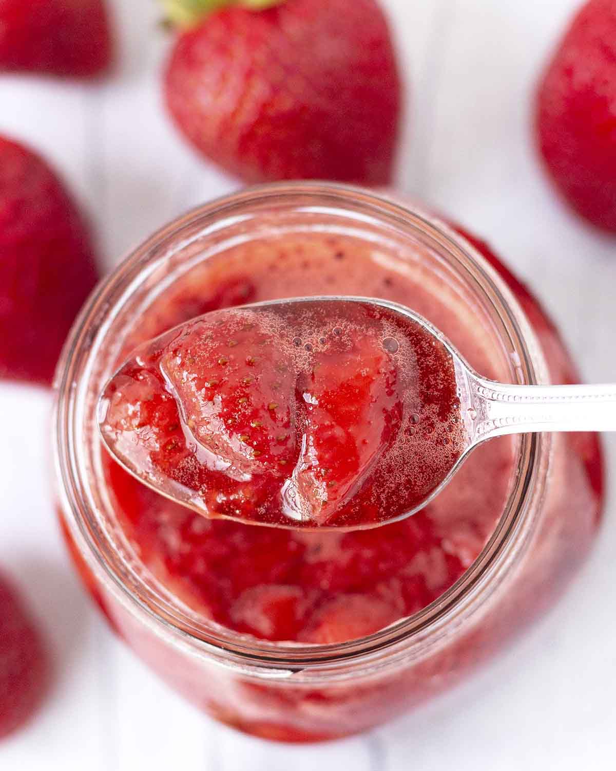 A spoon full of strawberry dipping sauce being held over a jar of the sauce.
