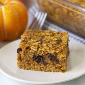 Image shows an egg-free baked pumpkin oatmeal slice on a white plate, a fork sits behind the plate.