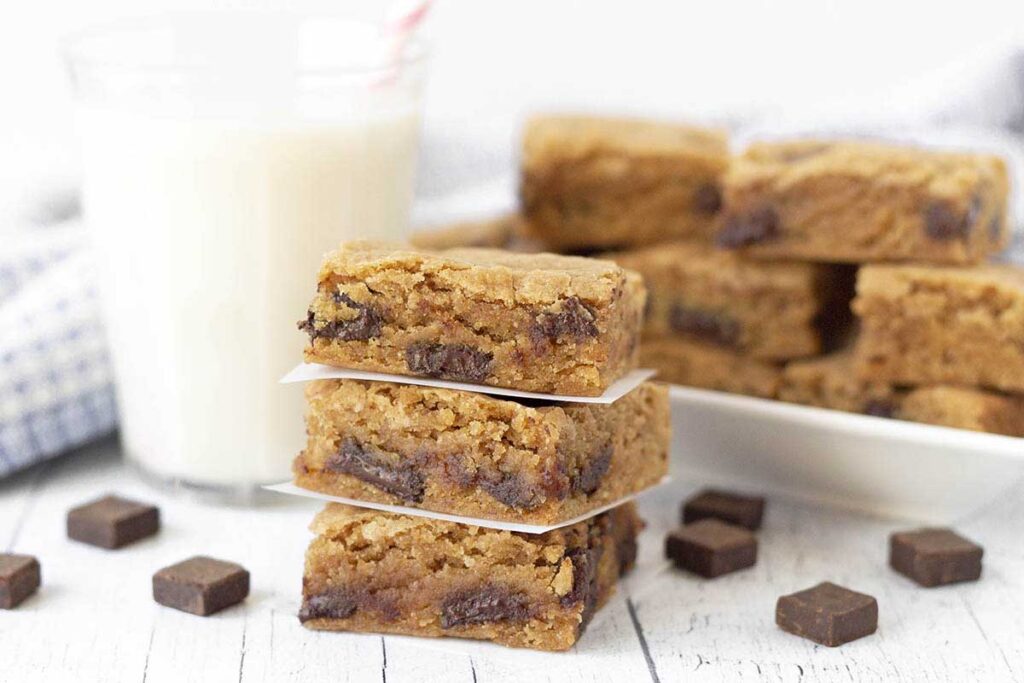 Three gluten free chocolate chip blondies squares stacked on top of each other and separated by parchment paper squares.