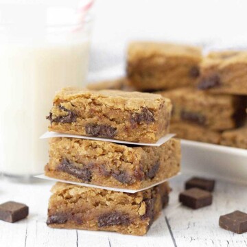 Three gluten free chocolate chip blondies squares stacked on top of each other and separated by parchment paper squares.