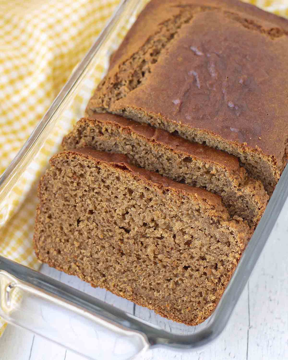 Freshly baked gluten free banana bread in a glass baking dish, there are two sliced pieces at the front of the loaf.