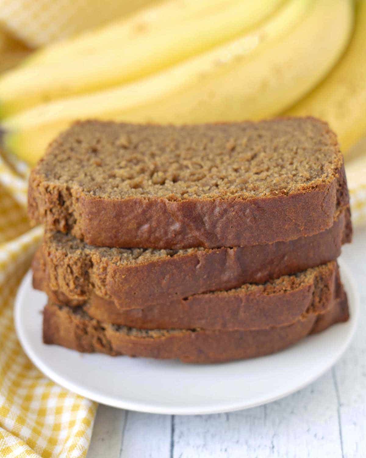 Four slices of eggless banana bread stacked on top of each other, slices are sitting on a white plate.