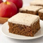 A square of frosted egg-free, gluten-free applesauce cake sitting on a white plate.