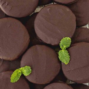 An overhead shot of many chocolate dipped mint cookies garnished with fresh mint leaves.