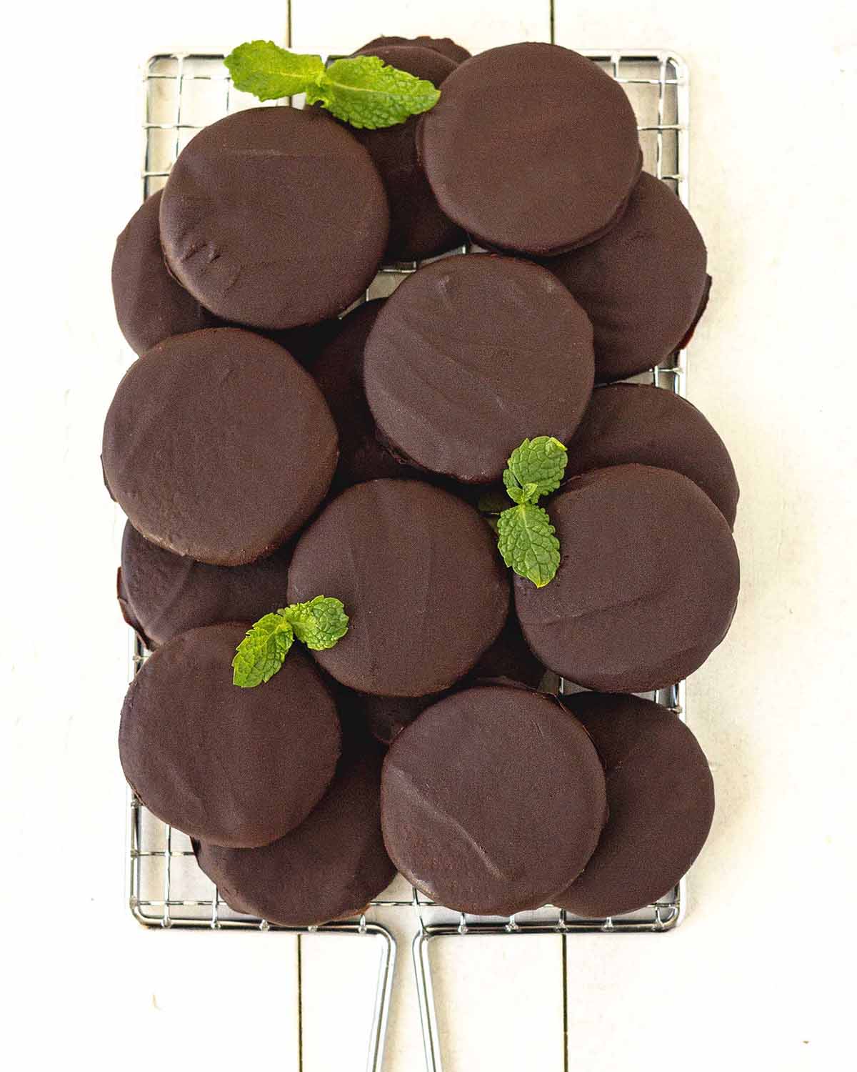 An overhead shot of gluten-free chocolate mint cookies sitting on a cooling rack, fresh mint leave are amongst the cookies.