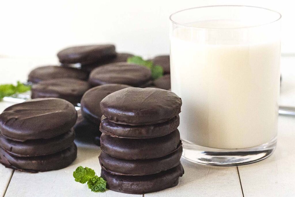 Several chocolate mint cookies on a white table, a glass of milk sits behind the cookies.