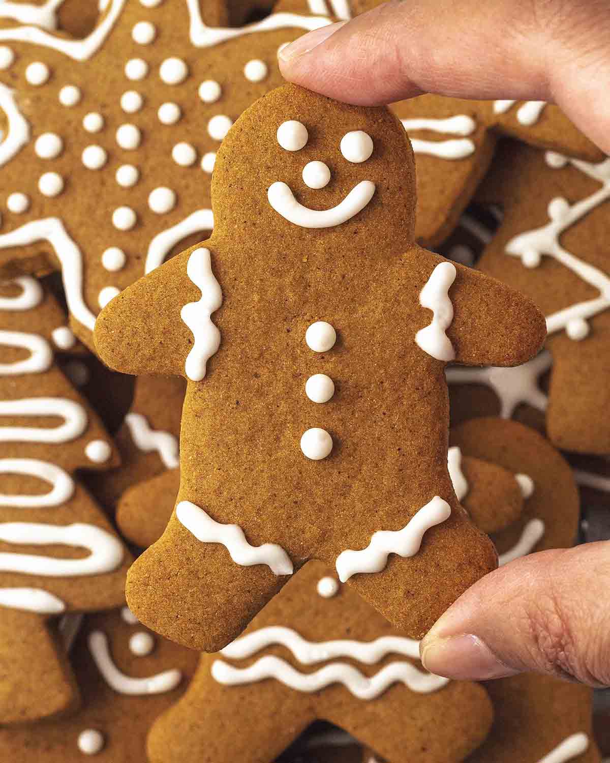A hand holding up a gingerbread man cookie that has been decorated with vegan royal icing.