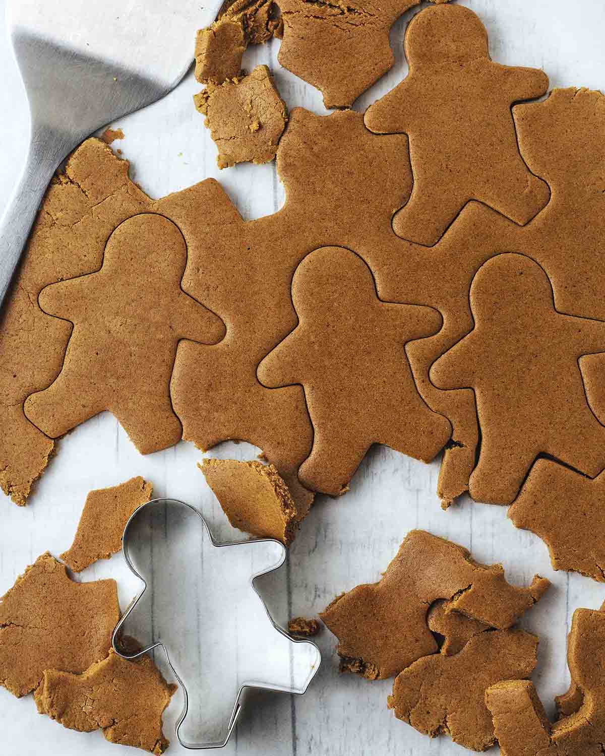 Rolled out gingerbread cookie dough on parchment paper with gingerbread people shapes cut out of the dough.