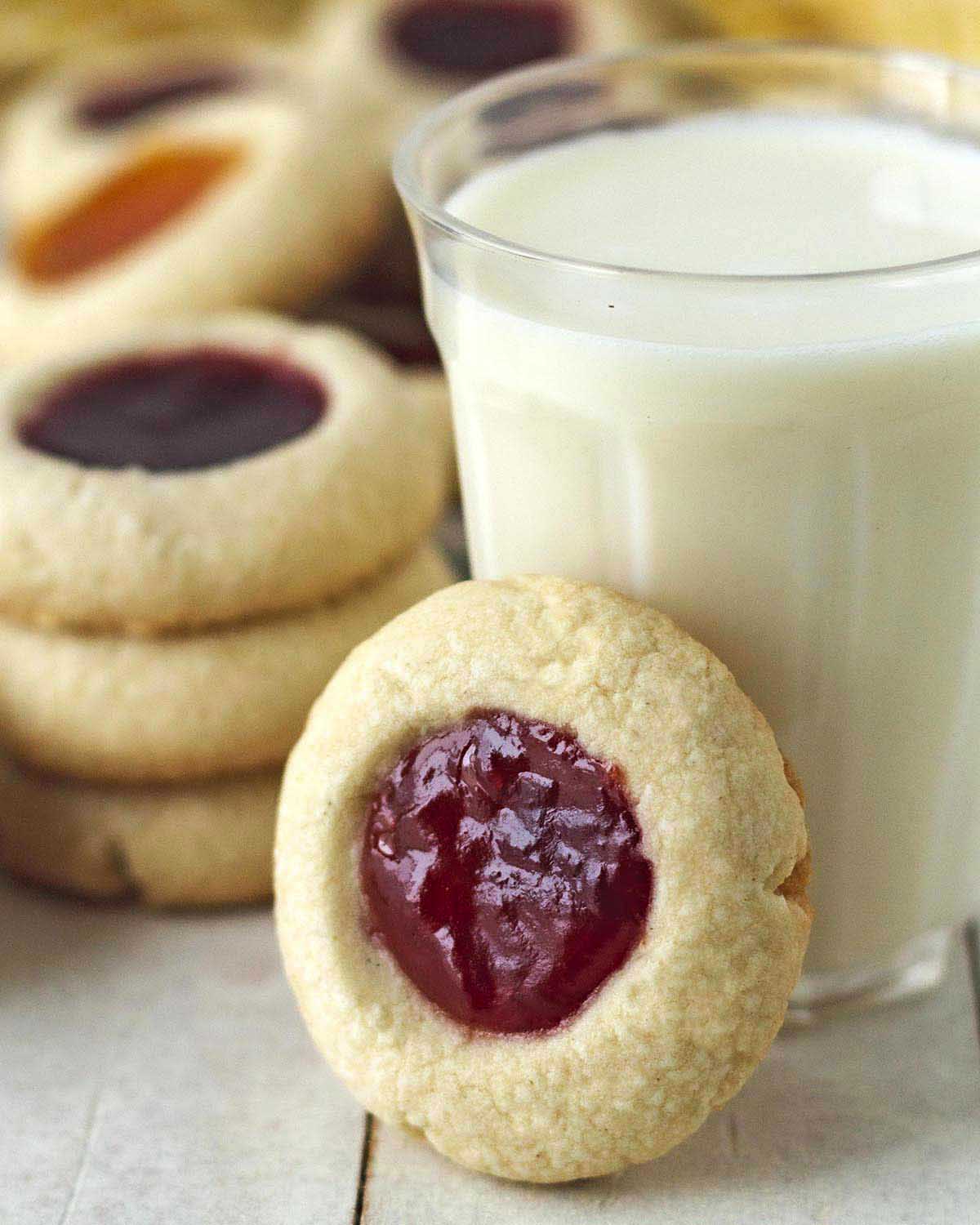An egg-free-, dairy-free raspberry thumbprint cookies leaning on a glass of almond milk.