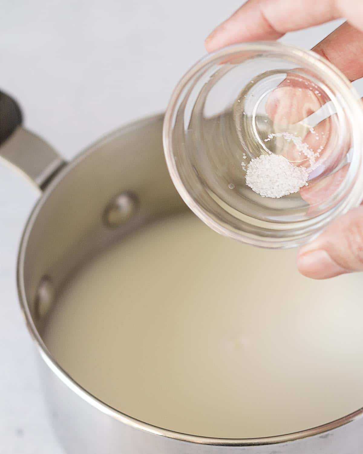 A hand adding a pinch of salt from a small glass bowl into a pot with milk and water to be used to make homemade oatmeal.