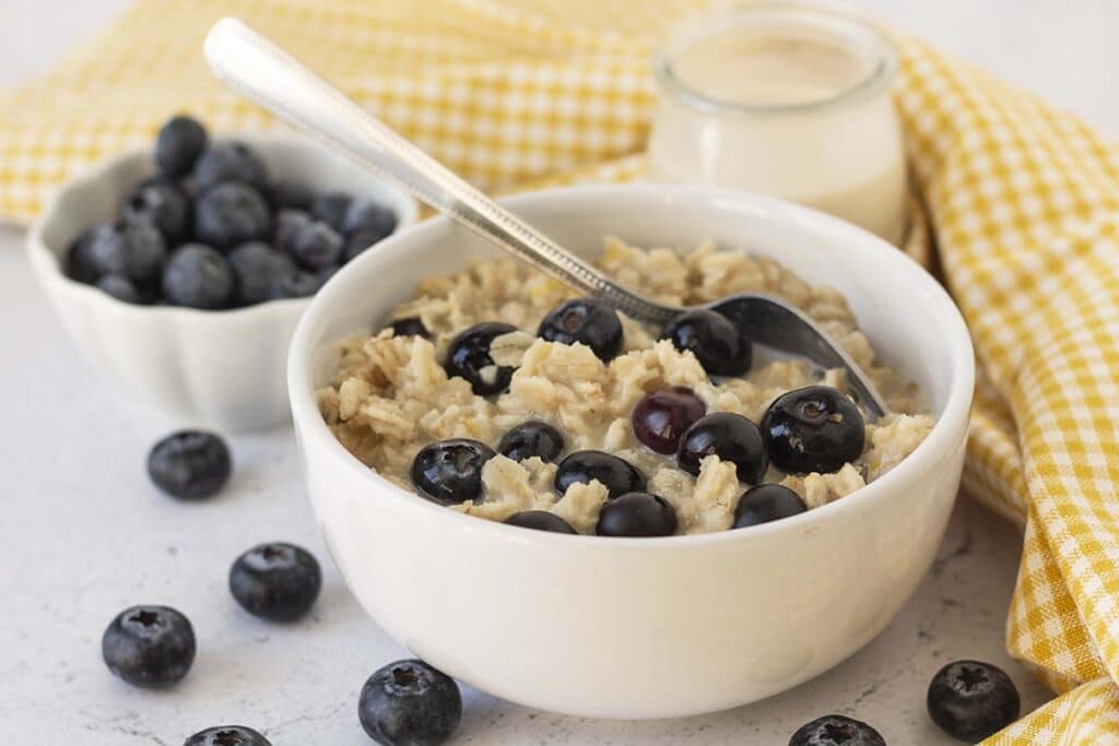 Blueberry oatmeal in a white bowl, the oatmeal is topped with extra blueberries and a spoon is in the bowl.