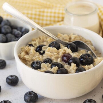 Blueberry oatmeal in a white bowl, the oatmeal is topped with extra blueberries and a spoon is in the bowl.