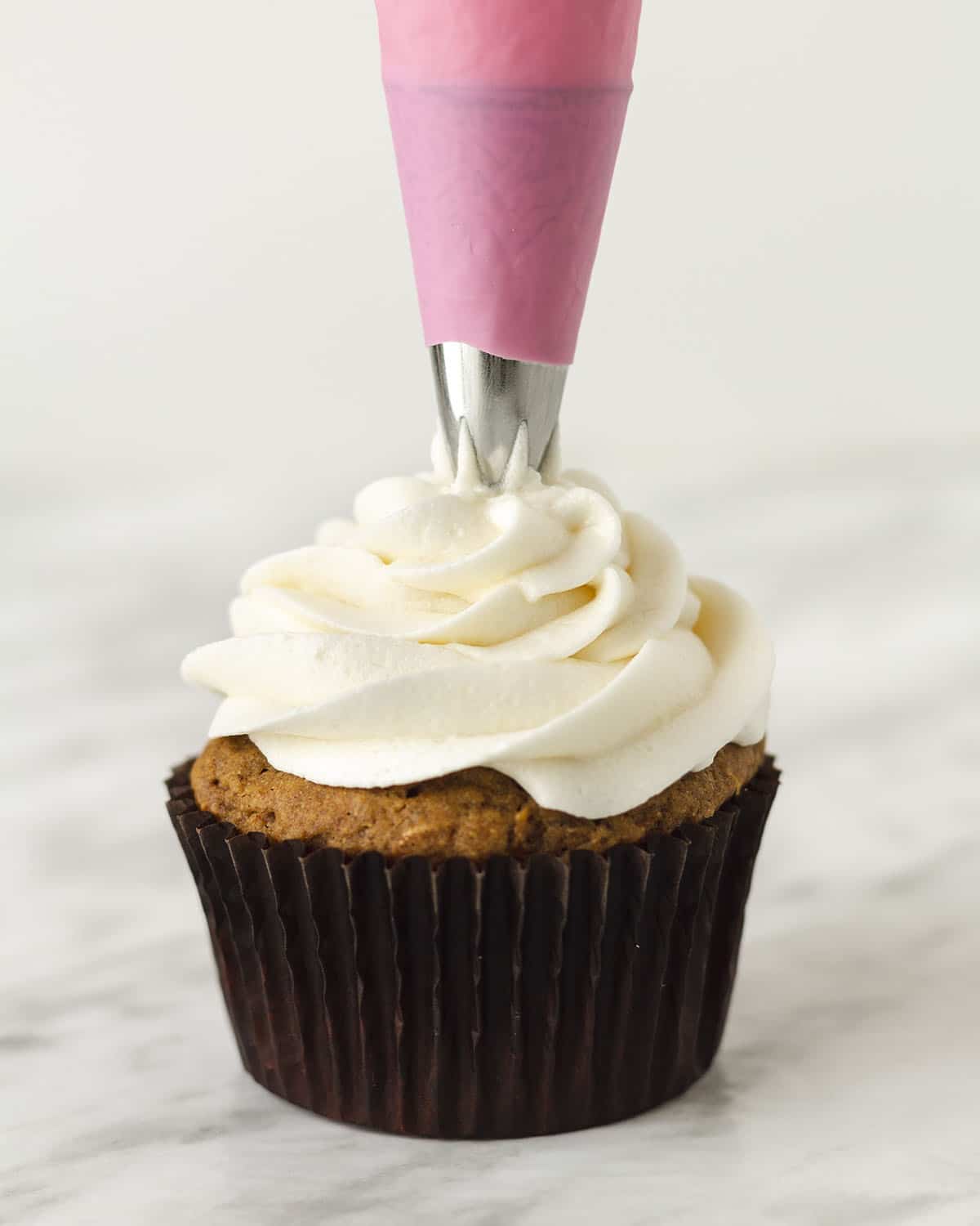 Dairy-free cream cheese icing being piped onto a carrot cupcake.