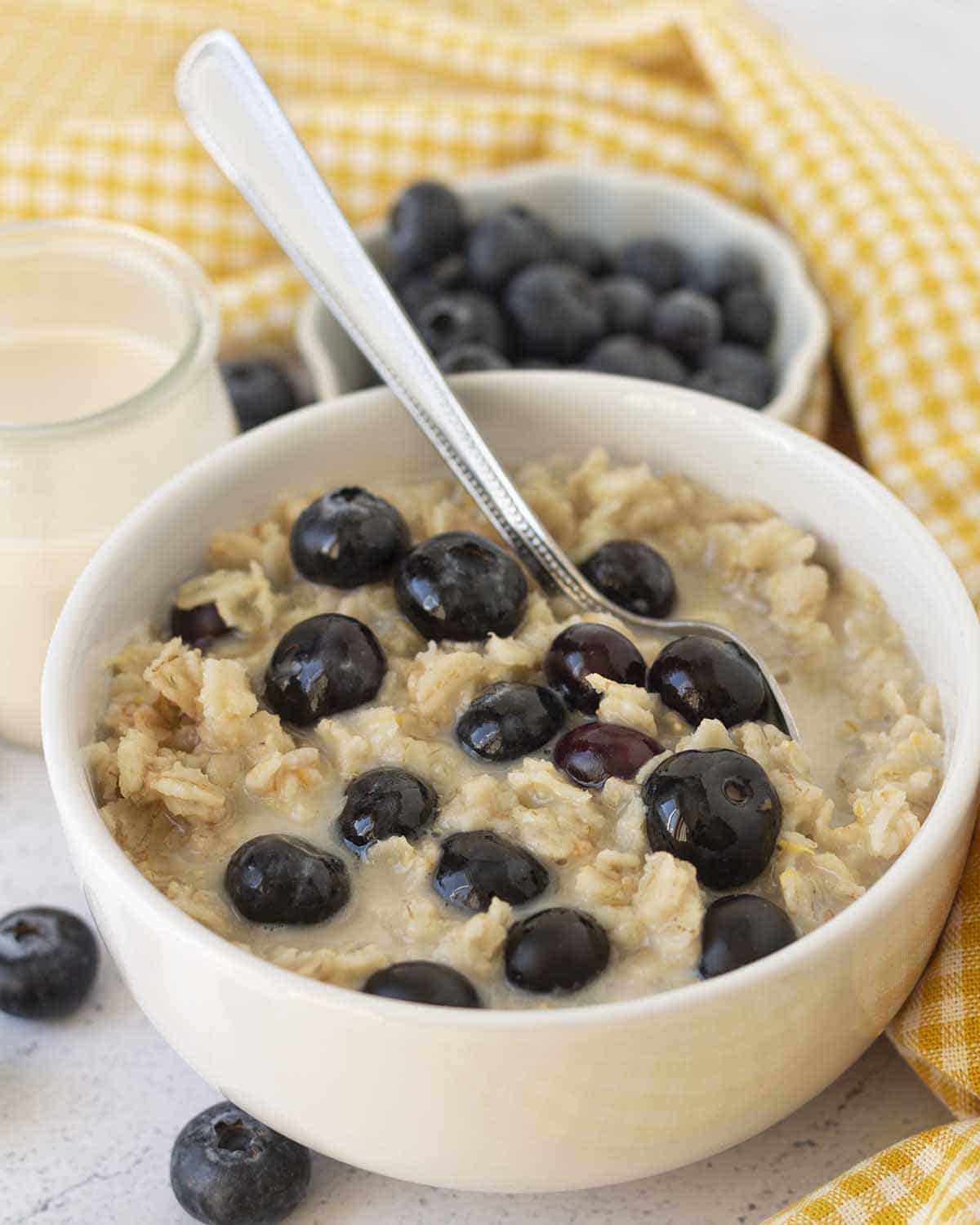 Image shows a white bowl sitting on a white table, the bowl is filled with lemon blueberry oatmeal.