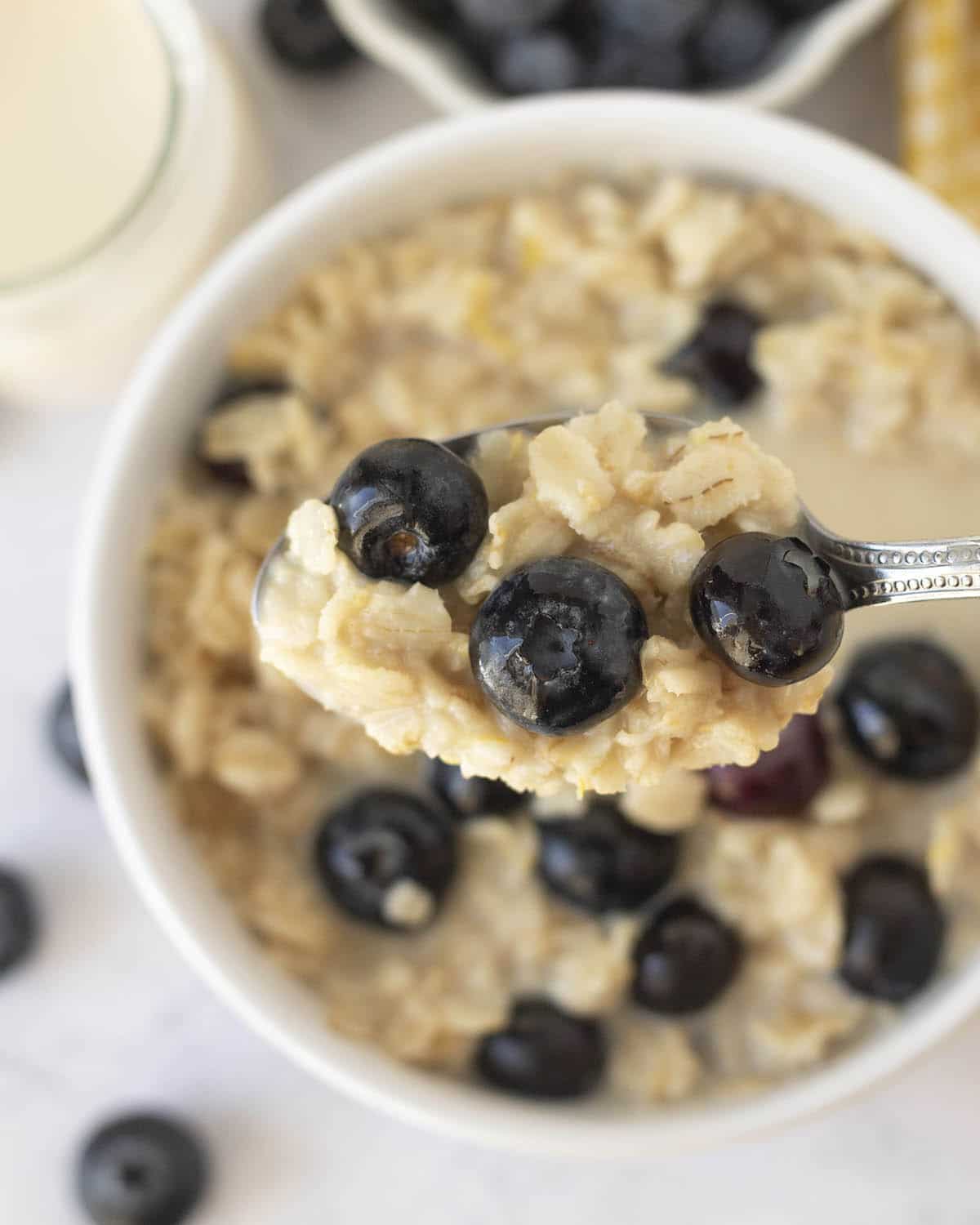 A spoonful of oatmeal and blueberries being held up above a full bowl of the same oatmeal.