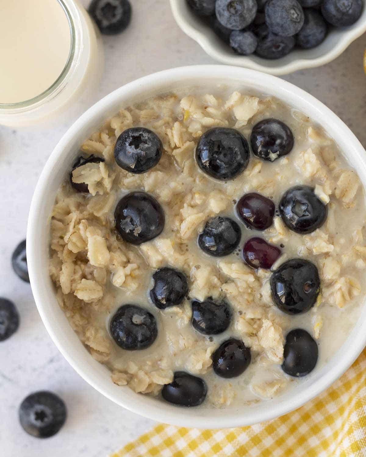 Vegan blueberry oatmeal in a white bowl with fresh blueberries on top.