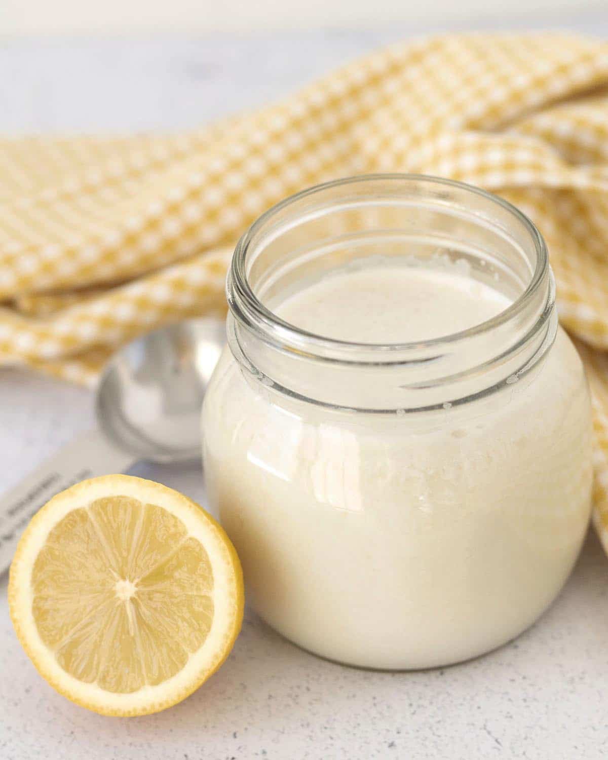 Image shows a jar full of dairy-free buttermilk, a fresh lemon and measuring spoon sits beside the jar.