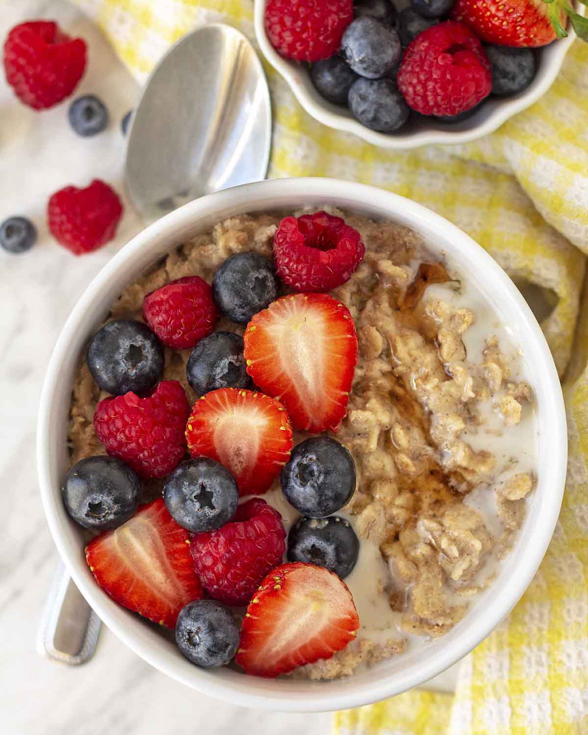 A bowl of flax oats in a white bowl with berries on top of the oats, a spoon sits to the left of the bowl.
