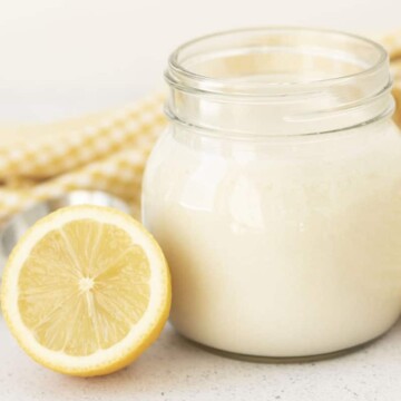Image shows a small mason jar filled with vegan buttermilk, half of a fresh lemon sits beside the jar.