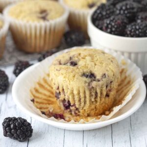 A dairy-free blackberry muffin on a plate with its muffin wrapper peeled down.