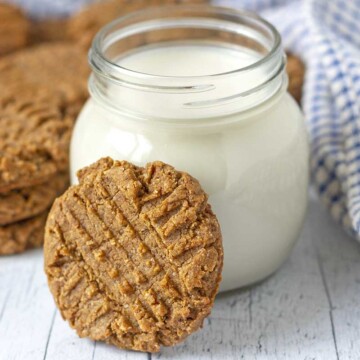 An eggless peanut butter cookie leaning against a small mason jar filled with almond milk.