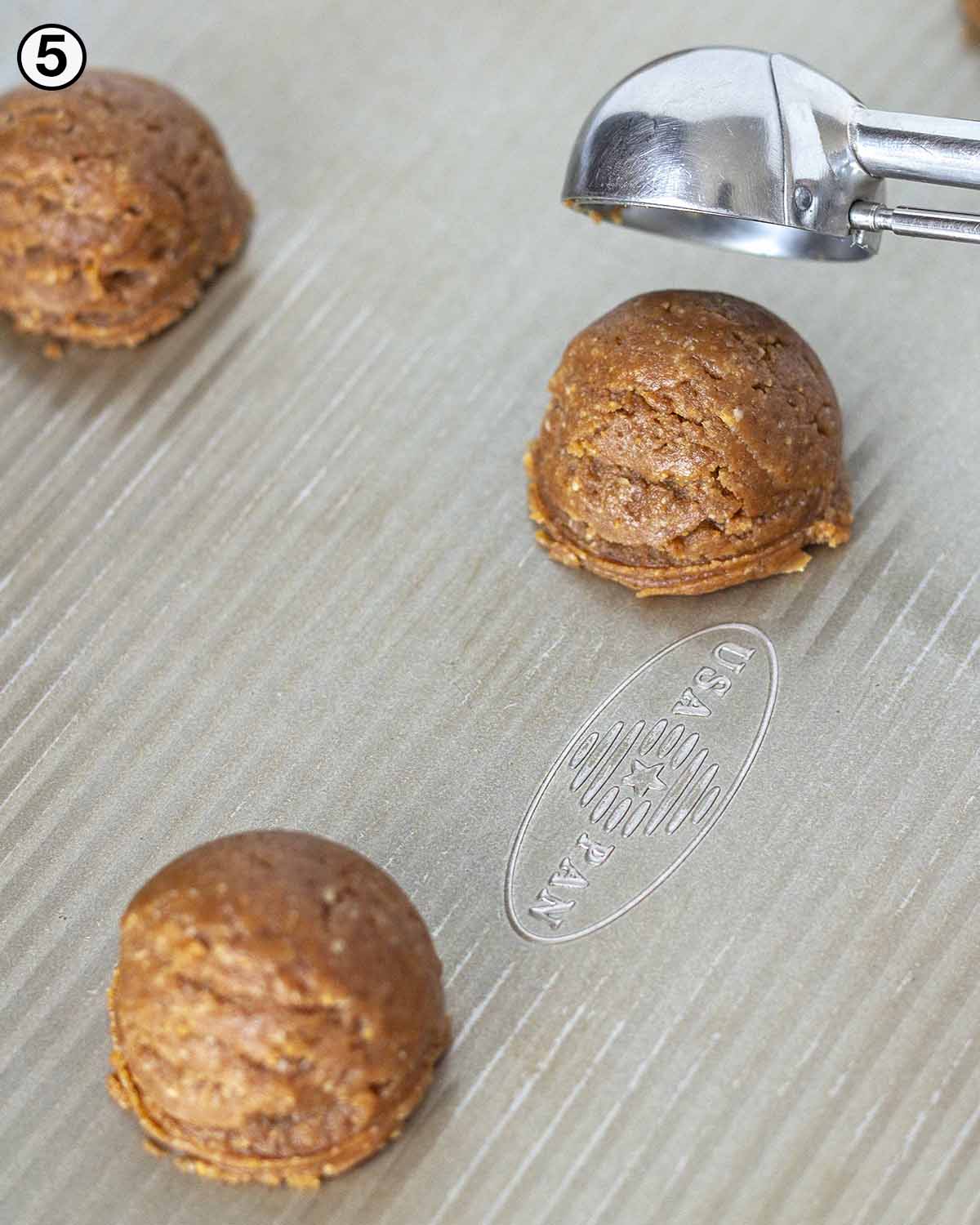 Vegan almond flour peanut butter cookies being put on a cookie sheet with a cookie scoop.