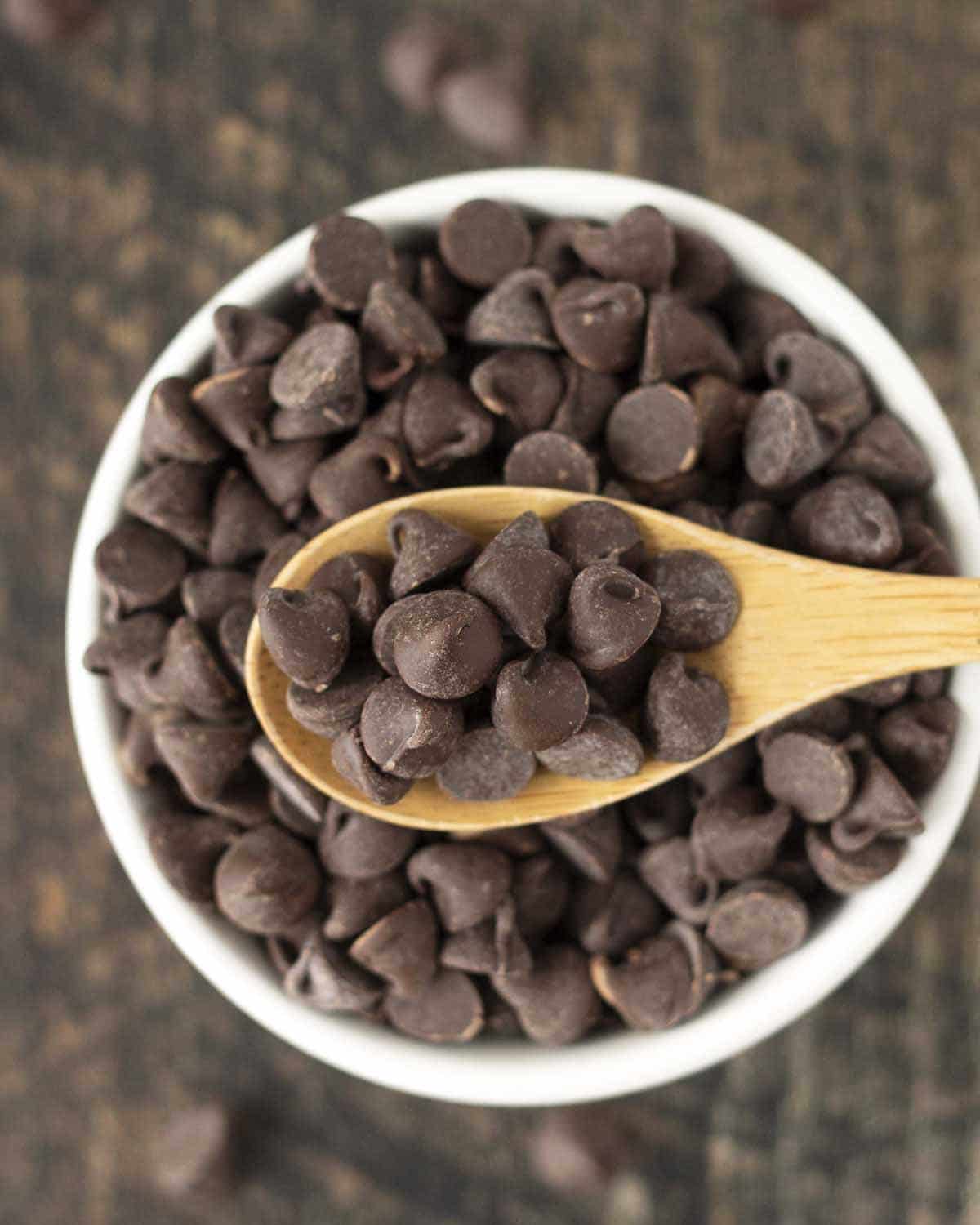 A spoon full of vegan chocolate chips being held over a bowl.